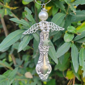 May include: A handcrafted angel ornament made from a vintage spoon. The angel features silver-toned wings, a pearl bead head, and a star charm. The ornament hangs from a silver wire loop, perfect for holiday decor.