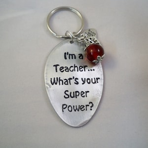 May include: A silver-colored metal keychain with the text "I'm a Teacher... What's your Super Power?" The keychain has a red bead and a small charm that says "Made with love".