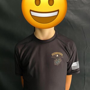 May include: A dark gray short-sleeved shirt with the text "FIDELIS DEFENSE" above an eagle and globe design. The shirt has a small American flag on the sleeve.