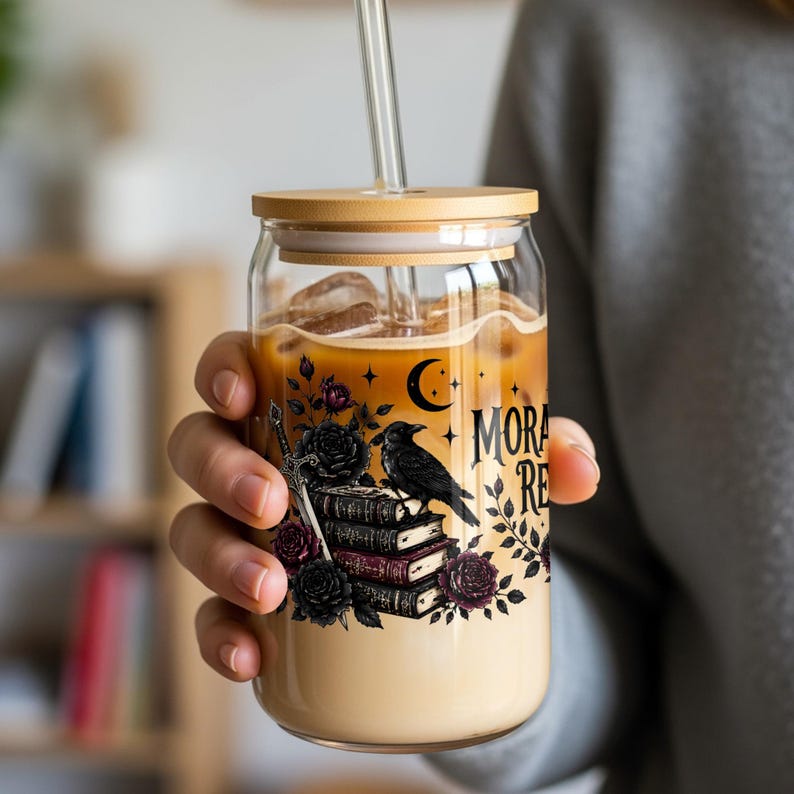 Glass tumbler with crow, roses, and books design, holding iced coffee.