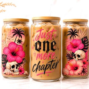 Puede incluir: Tres vasos de vidrio con tapas de bambú, llenos de café helado. Cada vaso presenta un diseño tropical con una calavera, flores de hibisco y palmeras. El vaso central tiene el texto "Just one more chapter".