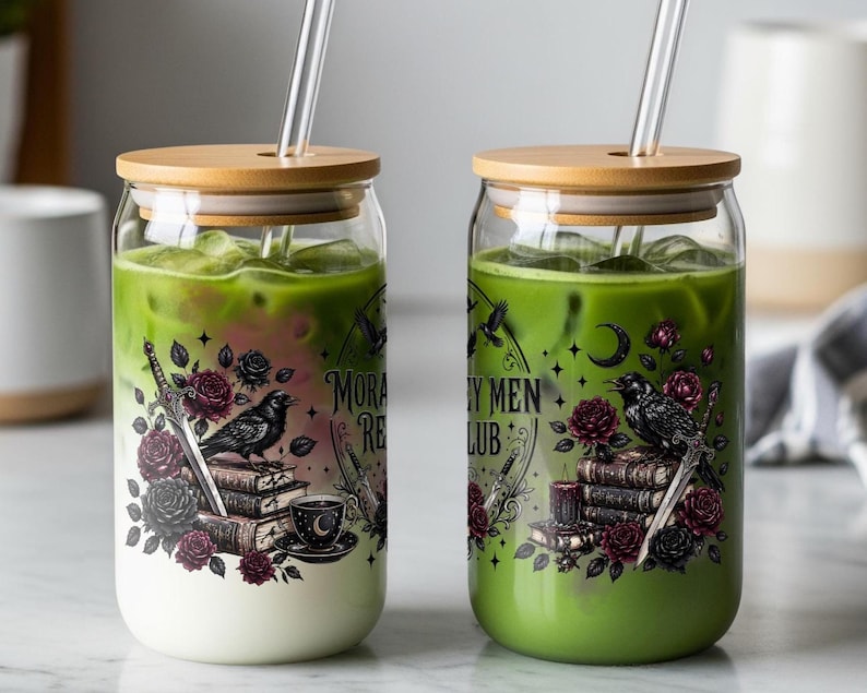 Two glass cups with straws, one with layered green tea and milk, the other with green tea, both with dark floral and book designs.