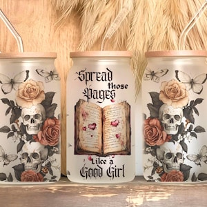 May include: Three glass tumblers with wooden lids and metal straws. The tumblers feature a design of skulls, roses, and butterflies. The center tumbler has the text "Spread those Pages Like a Good Girl" with an open book graphic.