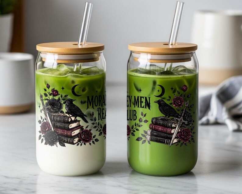 Two glass tumblers with straws, one white drink, one green, decorated with raven and book illustrations.