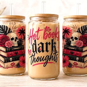 Può includere: Tre bicchieri di vetro con coperchi in legno e cannucce trasparenti, riempiti con una bevanda marrone chiaro. Ogni bicchiere presenta un disegno con un teschio, libri, fiori e il testo "Hot books dark thoughts."
