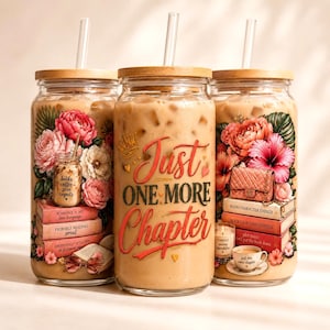 Op de afbeelding: Drie glazen bekers met houten deksels en doorzichtige rietjes, gevuld met een lichtbruine drank. Elke beker heeft bloemen- en boekenontwerpen met de tekst "Just One More Chapter."
