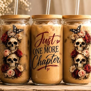 Puede incluir: Tres frascos de vidrio con tapas de madera, llenos de un líquido marrón claro y pajitas. Cada frasco está decorado con un diseño de calavera, flores y una mariposa. El frasco del medio tiene el texto "Just One More Chapter".