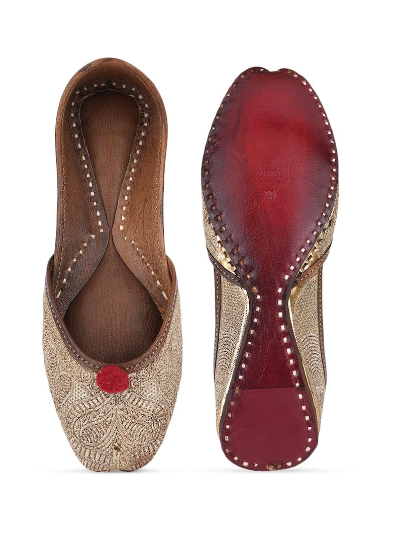 Pode incluir: Par de sapatos slip-on bordados dourados com um pompom vermelho e interior em couro castanho. A sola &eacute; vermelha com detalhes dourados. Os sapatos s&atilde;o exibidos em um fundo branco.