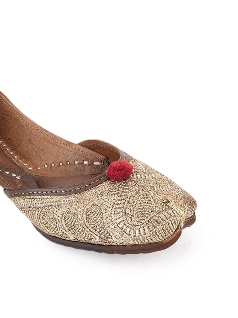 Pode incluir: Close-up de um sapato bordado dourado com um detalhe de pompom vermelho. O sapato apresenta padr&otilde;es intrincados e uma sola de couro castanho. O design &eacute; detalhado e o sapato parece ser feito &agrave; m&atilde;o.