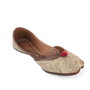 Pode incluir: Um sapato raso bordado dourado com bico fino. O sapato tem sola e acabamento em couro castanho, com um pequeno detalhe de pompom vermelho na ponta. O sapato &eacute; provavelmente de estilo tradicional.