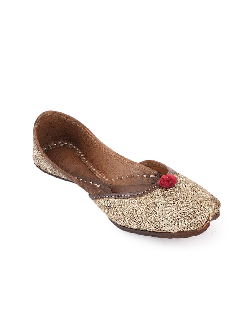 Pode incluir: Um sapato raso bordado dourado com bico fino. O sapato tem sola e acabamento em couro castanho, com um pequeno detalhe de pompom vermelho na ponta. O sapato &eacute; provavelmente de estilo tradicional.