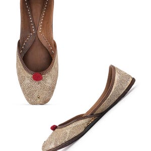 Pode incluir: Dois sapatos dourados bordados sem atacadores com um detalhe de pompom vermelho. Os sapatos t&ecirc;m interior e sola em couro castanho. Um sapato &eacute; visto de cima e o outro est&aacute; em &acirc;ngulo.