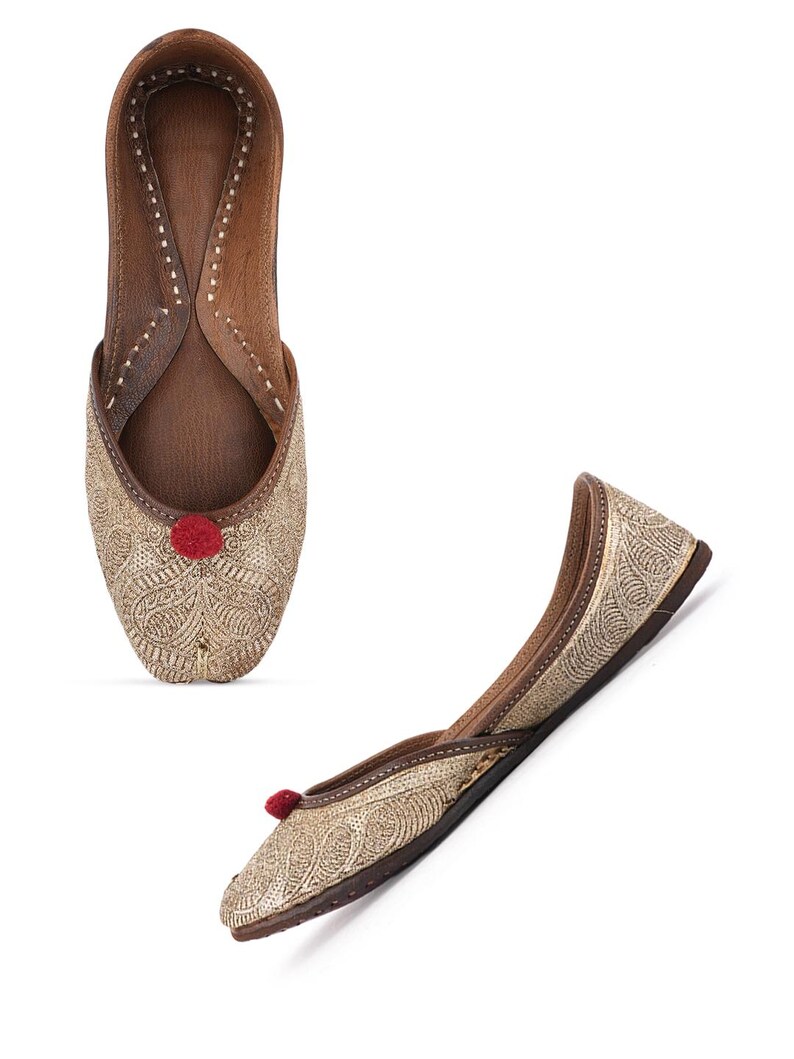 Pode incluir: Dois sapatos dourados bordados sem atacadores com um detalhe de pompom vermelho. Os sapatos t&ecirc;m interior e sola em couro castanho. Um sapato &eacute; visto de cima e o outro est&aacute; em &acirc;ngulo.