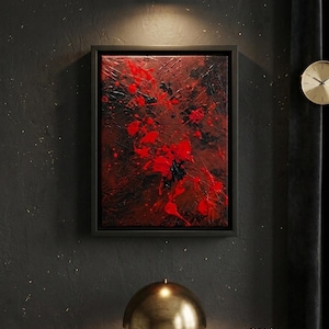 May include: Abstract art piece in a black frame. The artwork features a textured background with bold red paint splatters and black accents. The painting is displayed on a dark wall, illuminated by a brass-colored wall sconce and a table lamp.