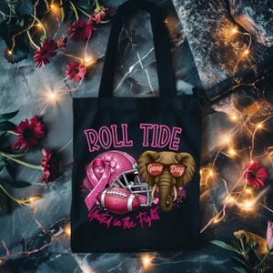 May include: Black tote bag with the text "ROLL TIDE" in pink. The bag features a pink football helmet, a football, and an elephant wearing sunglasses. The phrase "United in the Fight" is also on the bag.