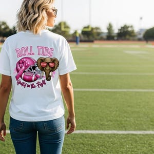 May include: White t-shirt with a pink graphic featuring a football helmet, a pink ribbon, and an elephant wearing sunglasses. The text "ROLL TIDE" and "United in the Fight" are also printed on the shirt.