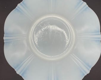May include: A vintage, opalescent glass plate with a scalloped edge and a light blue rim. The plate has a fluted design radiating from the center. The plate is round and has a smooth, glossy surface. A decorative piece for serving or display.