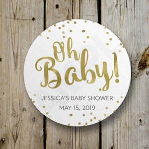 Op de afbeelding: Ronde witte sticker met gouden confetti en de tekst "Oh Baby!" in gouden schrift. Onder de tekst staat "Jessica's Baby Shower" en "May 15, 2019" in zwarte tekst.