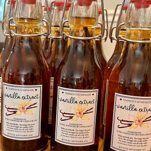 May include: Several glass bottles of vanilla extract with red stoppers and metal clasps. Each bottle has a white label with the text "TIMPSON'S HOMEMADE vanilla extract" and a floral illustration. The bottles are filled with a dark amber liquid.