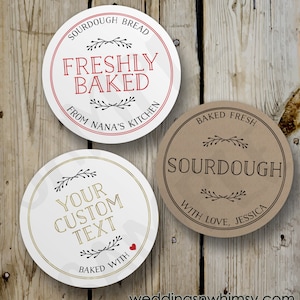 May include: Three round, white, paper labels with black text and gold accents. The first label says "Sourdough Bread Freshly Baked From Nana's Kitchen". The second label says "Your Custom Text Baked With". The third label says "Baked Fresh Sourdough With Love, Jessica".