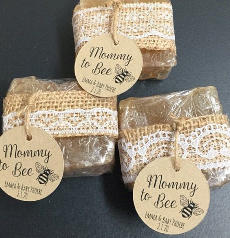 May include: Three clear, honey-colored soap bars wrapped in burlap and lace with a brown circle tag that reads "Mommy to Bee" with a bee illustration and the text "EMMA & BABY PHOEBE 2.1.20".