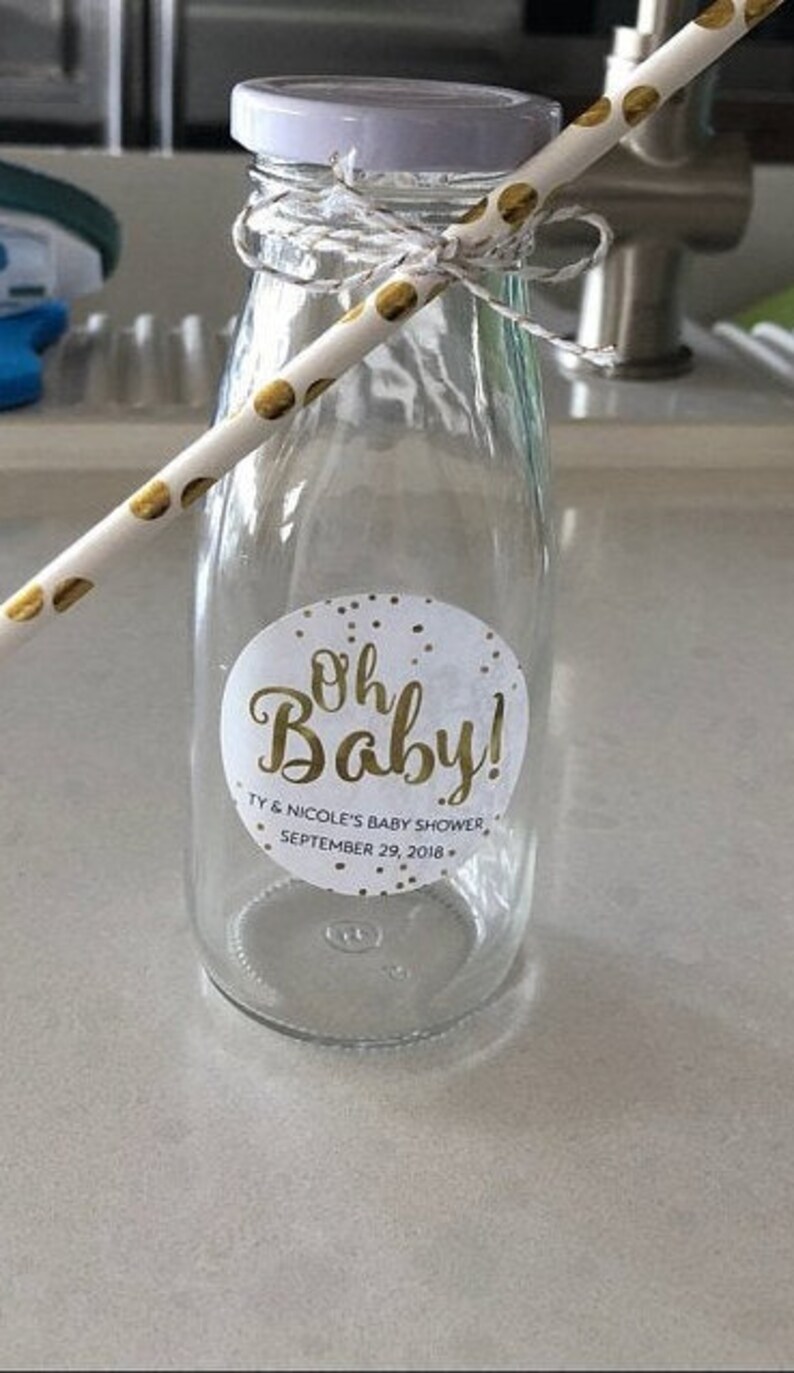 Op de afbeelding: Een heldere glazen fles met een wit deksel en een gouden rietje. De fles heeft een wit en gouden sticker met de tekst "Oh Baby!" met de tekst "Ty & Nicole's Baby Shower September 29, 2018."