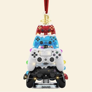 May include: A Christmas tree ornament made of stacked game controllers in red, blue, white, and black. The ornament has a gold PlayStation logo at the top and the name "DAVID" at the base. The ornament is decorated with faux snow and colorful lights.
