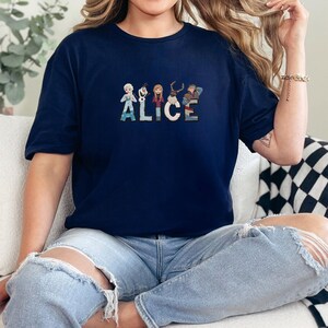 Może przedstawiać: Granatowa koszulka z haftowanym imieniem "ALICE" w kolorowych literach. Każda litera przedstawia postać z popularnego filmu animowanego. Wygodny, swobodny styl.