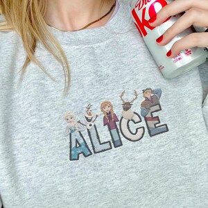 Może przedstawiać: Jasnoszara bluza z napisem "ALICE" z postaciami z filmu Kraina Lodu. Postacie to Elsa, Olaf, Anna, Sven i Kristoff. Bluza wykonana jest z miękkiego materiału.