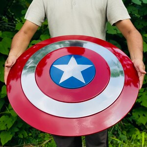 May include: A circular shield in red, white, and blue, featuring a white star on a blue central disc. The shield has a shiny surface and a design inspired by a superhero's iconic emblem.