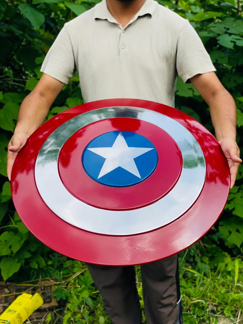 May include: A circular shield in red, white, and blue, featuring a white star on a blue central disc. The shield has a shiny surface and a design inspired by a superhero's iconic emblem.