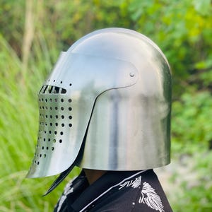 K&ouml;nnte beinhalten: Ein polierter silberner Ritterhelm mit Visier und Bel&uuml;ftungsl&ouml;chern. Der Helm dient zum Schutz von Kopf und Gesicht. Der Helm ist ein historischer Gegenstand, wahrscheinlich f&uuml;r Kost&uuml;m oder Ausstellung.