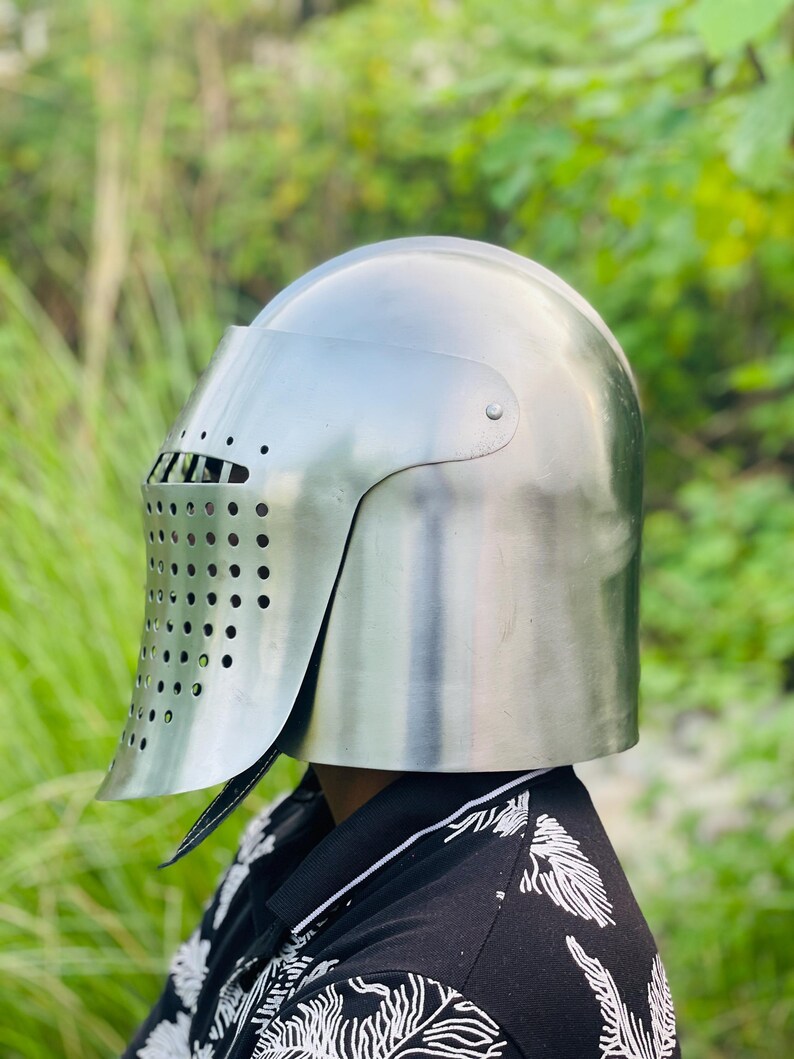 K&ouml;nnte beinhalten: Ein polierter silberner Ritterhelm mit Visier und Bel&uuml;ftungsl&ouml;chern. Der Helm dient zum Schutz von Kopf und Gesicht. Der Helm ist ein historischer Gegenstand, wahrscheinlich f&uuml;r Kost&uuml;m oder Ausstellung.