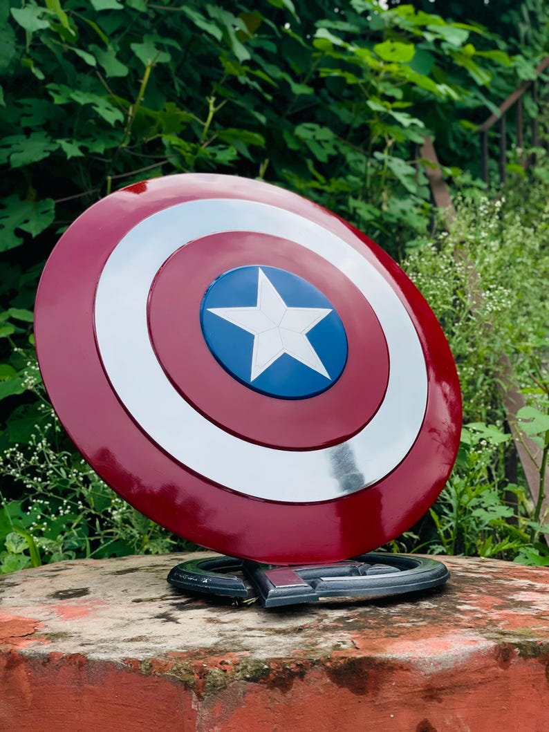 May include: A Captain America shield, with a red, white, and blue design. The shield has a central blue circle with a white star, encircled by white and silver rings. It is mounted on a stand, showcasing its iconic design.