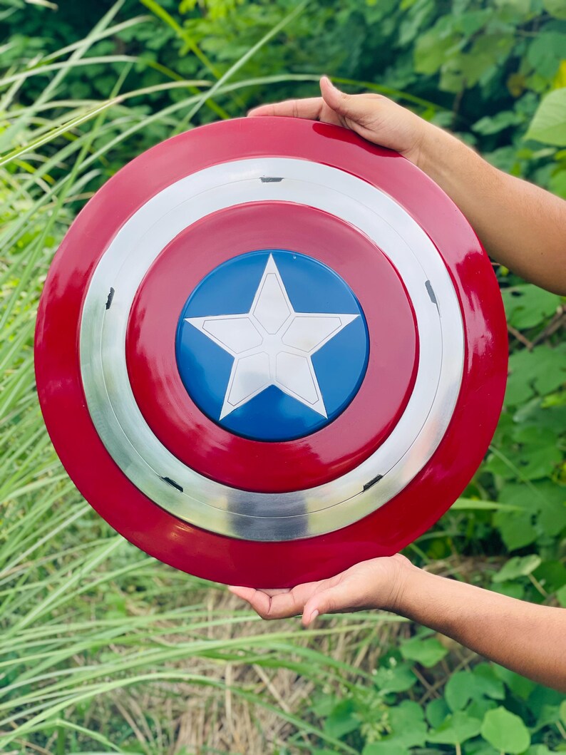 May include: A Captain America shield in red, white, blue, and silver. The shield features a red outer ring, a silver middle ring, and a blue centre with a white star. The round shield appears to be made of metal.