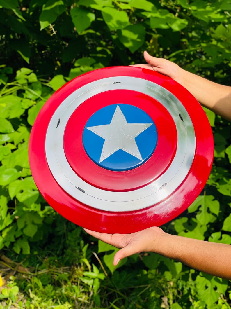 May include: A circular shield in red, white, and blue, featuring a central blue circle with a white star. The design includes a silver band separating the red and blue areas. A classic superhero accessory.