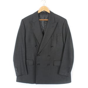 Peut inclure: Un blazer croisé gris anthracite suspendu à un cintre en bois. Le blazer a un revers cranté, deux rangées de boutons et deux poches avant. Les manches ont des boutons aux poignets. La veste est en tissu texturé.