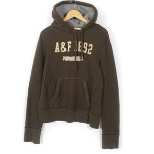 May include: A brown hoodie with a grey interior hood and a front pocket. The hoodie displays the text "A&F 1892" in a cream-coloured, slightly distressed font. The garment is hanging on a wooden hanger.