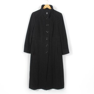 May include: A full-length black coat with a button closure and a high collar is suspended from a wooden hanger. The coat features a tailored silhouette, long sleeves, and a dark fabric, possibly a wool blend. The coat measures approximately 130 cm in length.