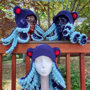 May include: Three crocheted octopus hats in blue and purple with red accents. The hats are on display on a wooden railing.