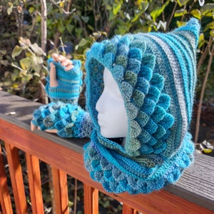 May include: A blue and green crocheted hooded cowl and fingerless gloves with a scale pattern.