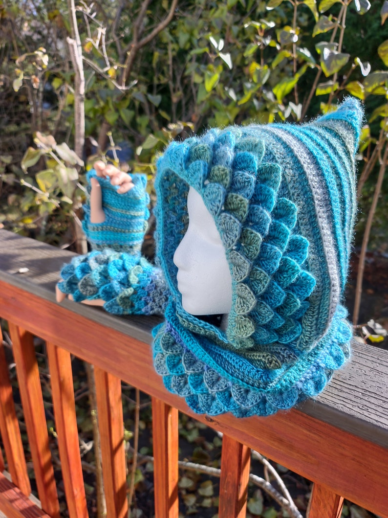 May include: A blue and green crocheted hooded cowl and fingerless gloves with a scale pattern.