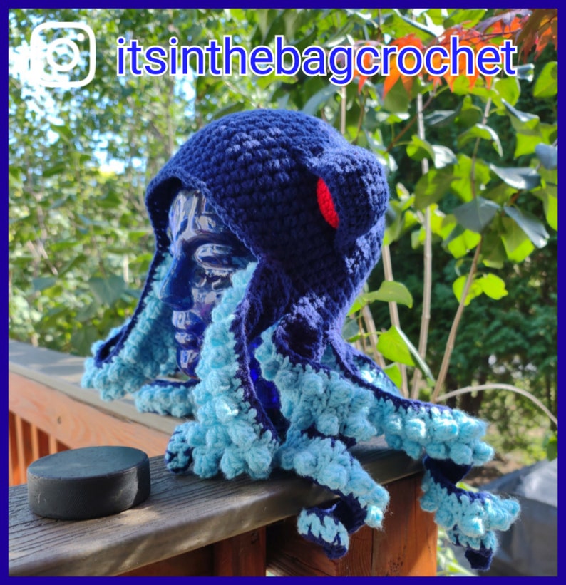 May include: Blue and turquoise crocheted octopus hat with a red pom-pom on top. The hat is on a mannequin head and is sitting on a wooden railing. The text "itsinthebagcrochet" is visible in the top right corner of the image.