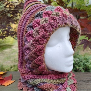 May include: A crocheted hooded cowl with a textured, scale-like pattern in shades of pink, brown, green, and purple.