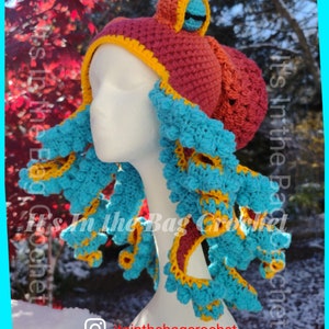 May include: A handmade crochet octopus hat in shades of burgundy, orange, yellow, and turquoise blue. The hat features a head with two eyes and multiple tentacles. The text "It's In The Bag Crochet" and the Instagram handle "itsinthebagcrochet" are visible.