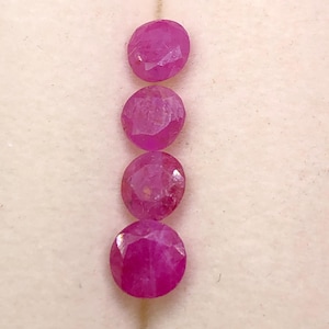 May include: Four round, faceted, vibrant pinkish-red rubies arranged in a vertical column. Each gemstone displays a polished, multi-faceted surface that reflects light, showcasing a deep, saturated color and a circular cut with distinct edges.