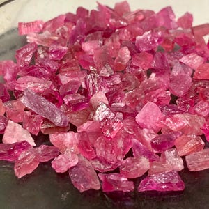 Peut inclure: Une collection de petits fragments de pierres précieuses brutes et non polies dans diverses nuances de rose vif, magenta et fuchsia profond. Les pièces présentent des bords irréguliers et dentelés ainsi que des surfaces translucides.
