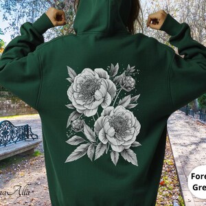 K&ouml;nnte beinhalten: Dunkelgr&uuml;ner Kapuzenpullover mit einem schwarz-wei&szlig;en Blumendruck von Pfingstrosen und Bl&auml;ttern auf dem R&uuml;cken. Der Kapuzenpullover hat eine Kapuze und lange &Auml;rmel. Der Text "Forest Green" befindet sich in einem wei&szlig;en Kreis.