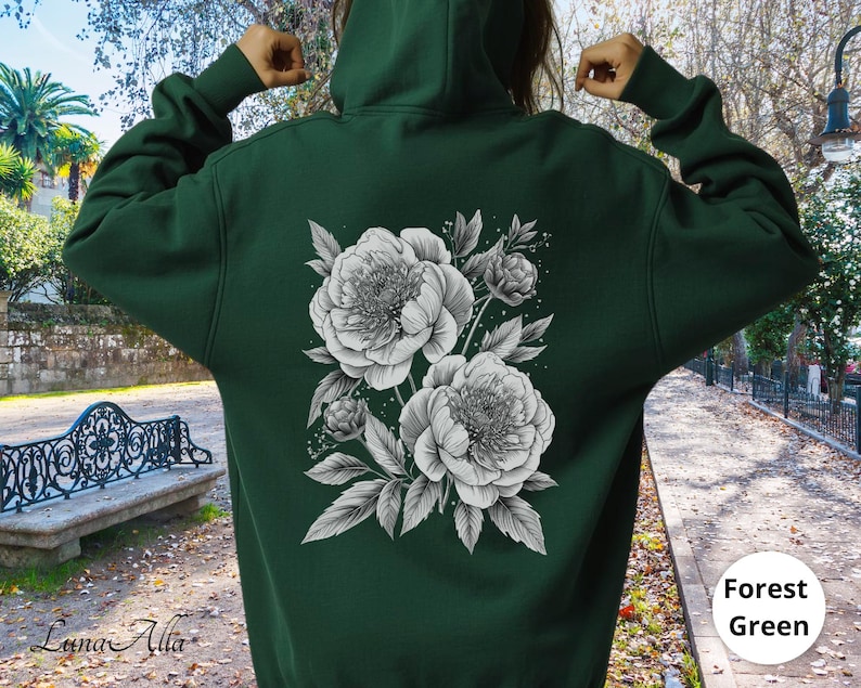 K&ouml;nnte beinhalten: Dunkelgr&uuml;ner Kapuzenpullover mit einem schwarz-wei&szlig;en Blumendruck von Pfingstrosen und Bl&auml;ttern auf dem R&uuml;cken. Der Kapuzenpullover hat eine Kapuze und lange &Auml;rmel. Der Text "Forest Green" befindet sich in einem wei&szlig;en Kreis.