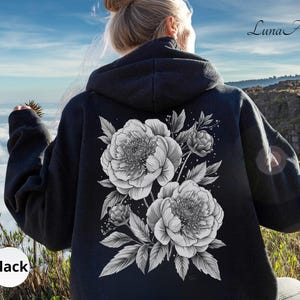 K&ouml;nnte beinhalten: Schwarzer Kapuzenpullover mit einem graustufigen Blumendesign auf dem R&uuml;cken, das Pfingstrosen und Bl&auml;tter zeigt. Das Wort "Black" ist unten links aufgedruckt. Der Markenname "Luna Alla" ist oben rechts aufgedruckt.